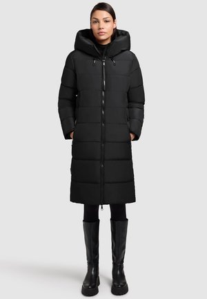 Zwarte pufferjas met een capuchon, voorzien van een ritsluiting, gewatteerd ontwerp en zijzakken. Gekozen met zwarte legging en kniehoge laarzen.