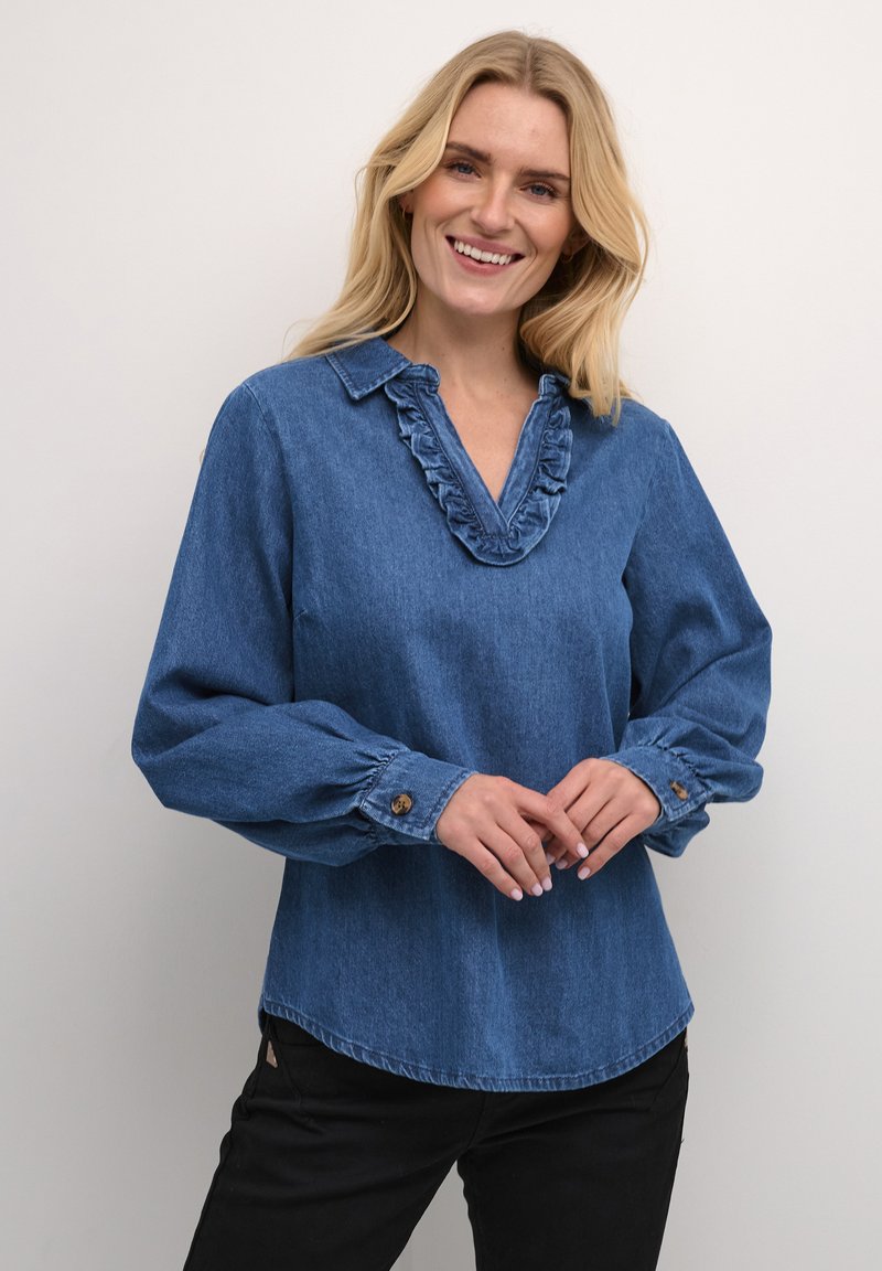 Camicia di jeans blu scuro con scollatura a V arricciata, maniche lunghe con polsini abbottonati e vestibilità rilassata. Texture morbida e design informale.