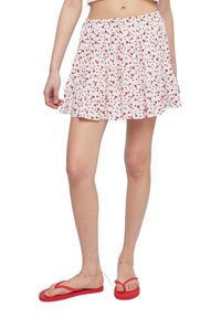 Gonna floreale bianca con motivo a rose rosse, cintura elastica arricciata, orlo a strati a volant, abbinata a infradito rosse e catena alla caviglia.