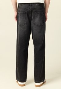 Svarta denimjeans med avslappnad passform, med två bakfickor och rak bendesign. Materialet verkar gediget med en lätt struktur.