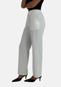 Witte, rechte broek met een soepele textuur, elastische tailleband en voorplooien. Gecombineerd met zwarte, puntige hakken.
