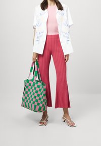 Camicetta bianca a maniche corte con fiori ricamati, top rosa a coste, pantaloni rosa plissettati e una borsa a tracolla a quadri verdi e rosa, abbinata a sandali bianchi.