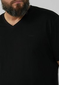 Black V-neck T-shirt made from cotton, featuring a subtle logo in black. The fabric appears smooth with short sleeves and a relaxed fit.