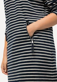 Vestido de forro polar con rayas horizontales en azul marino y crema, bolsillos con cremallera y borlas, y un corte holgado con mangas hasta los codos.
