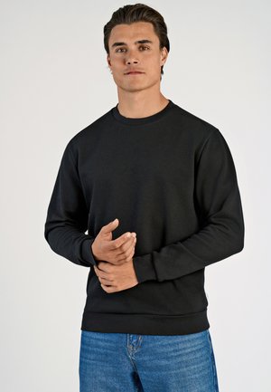 Zwarte sweatshirt met lange mouwen en een ronde halslijn, gemaakt van zachte stof, met ribbelmanchetten en -zoom. Draag over blauwe jeans.