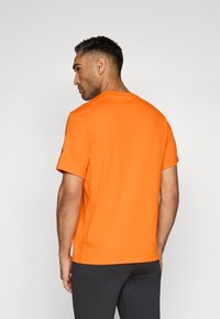 Camiseta de manga corta de color naranja brillante con cuello redondo, textura de tela suave y detalles en la costura del hombro. Acento negro en la manga.