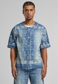 Denim shirt with short sleeves, light blue color, bandana print pattern, front button closure, and contrasting white stitching details.