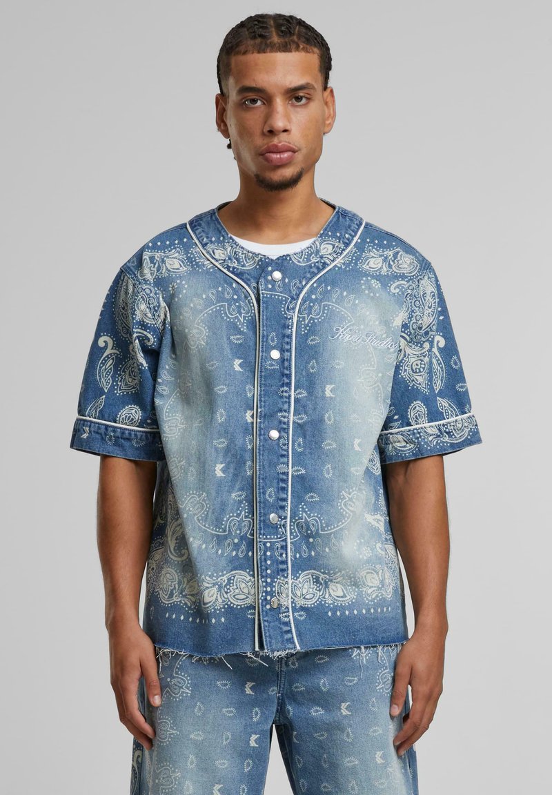 Denim shirt with short sleeves, light blue color, bandana print pattern, front button closure, and contrasting white stitching details.