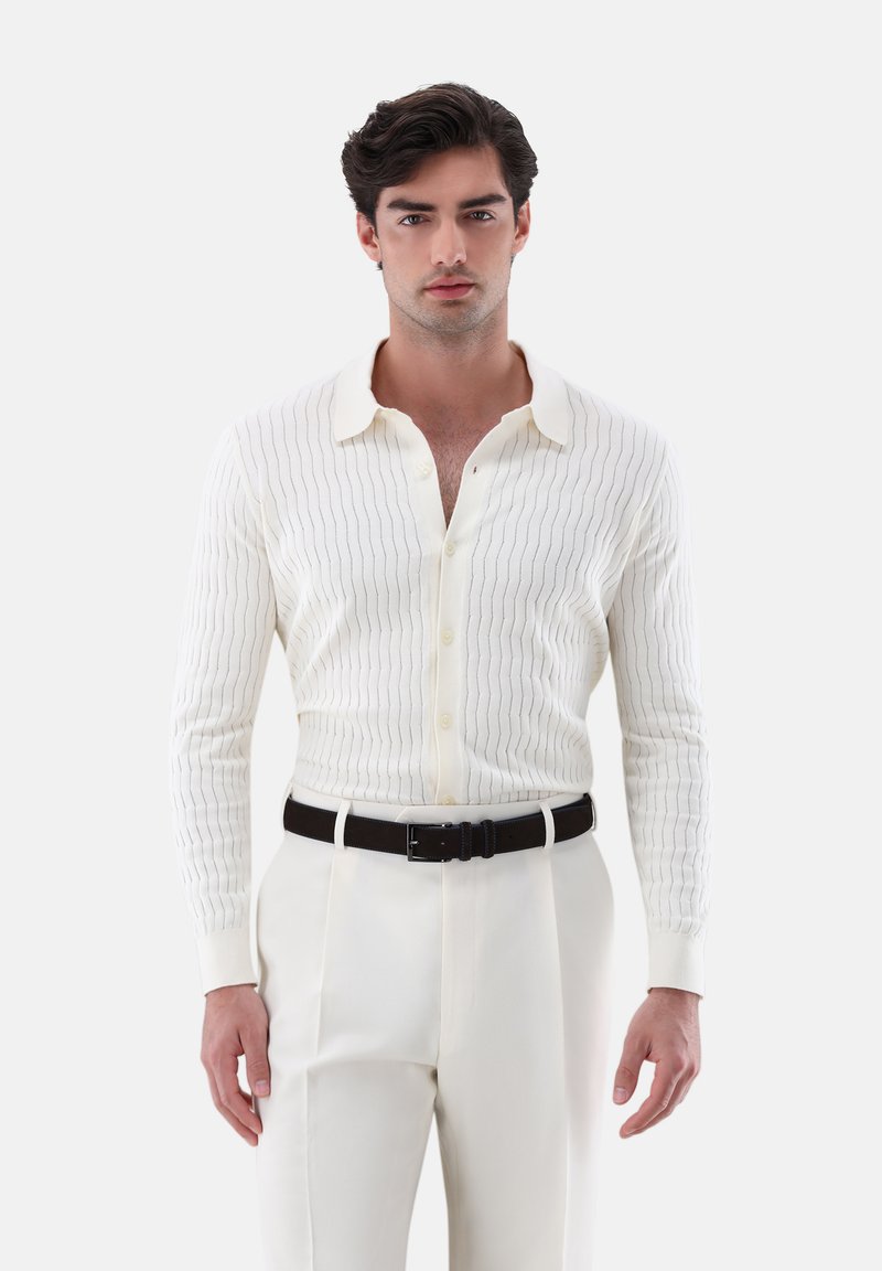 Weißes geripptes Strickhemd mit dezenten vertikalen Streifen, Button-Down-Kragen und langen Ärmeln, kombiniert mit cremefarbenen Hosen und einem schwarzen Gürtel.