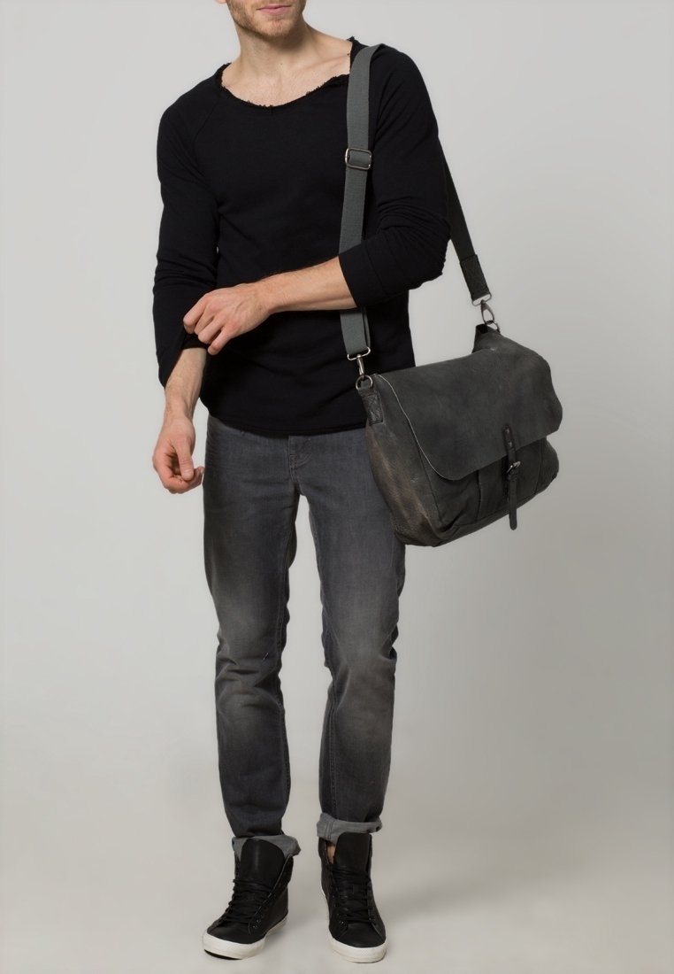 Chemise noire à manches longues avec un col usé, jeans gris, baskets noires et un sac messager en cuir gris avec rabat et boucle.