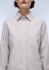 Striped button-up shirt featuring a soft fabric in beige and white, a classic collar, and a chest pocket, showcasing a straight cut.