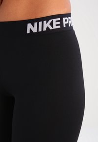 Czarne, dopasowane legginsy sportowe z szerokim pasem z napisem "NIKE PRO" białą czcionką. Gładka faktura i elastyczny materiał.