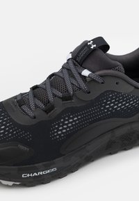 Scarpa sportiva nera con tomaia in rete, collo imbottito, dettagli riflettenti e suola in gomma texturizzata, con il marchio "CHARGE3" sul lato.
