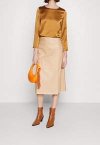 Langærmet bronzefarvet satin-top, beige faux læder midi-nederdel, orange buet håndtaske og brune ankelstøvler med firkantet tå.