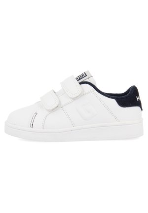 Baskets blanches avec un dessus en cuir lisse, fermetures velcro, talon bleu marine contrastant et une semelle blanche texturée. Présente des détails de couture minimaux.