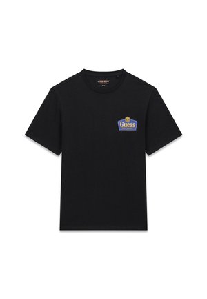 T-shirt en coton noir avec un patch logo Guess bleu et doré sur la poitrine gauche. Manches courtes et col rond. Texture lisse.