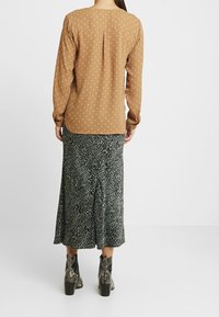 Blusa marrone a maniche lunghe con pois bianchi, abbinata a una gonna maxi a stampa leopardo verde e stivali neri con tacco con motivi a serpente.