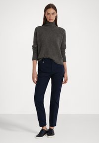 Maglione grigio a collo alto con costine, vestibilità ampia. Pantaloni blu navy su misura con gamba dritta e tasche frontali discreet. Sneakers nere completano il look.