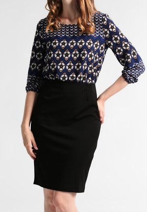 Blusa a fantasia navy con maniche tre quarti abbinata a una gonna a tubino nera. La blusa presenta design geometrici e floreali.