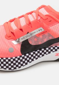 Scarpa da trail running Nike con tomaia in rete rosa, logo Swoosh nero, dettagli riflettenti e suola con motivo a scacchi.
