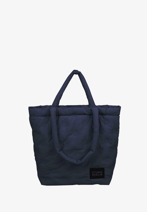 Marineblå quilten tote bag med to robuste, runde håndtak og rektangulær form. Har en liten svart etikett med teksten "STUDIO BERLIN".