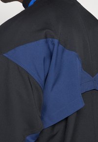 Black and blue garment featuring a layered design with a distinct blue accent on the shoulder, made of a smooth, lightweight fabric.