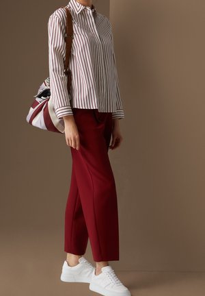 Weiß gestreifte Bluse mit Kragen, kombiniert mit burgunderfarbenen Hosen. Weiße Sneakers und eine mehrfarbige Handtasche runden das Outfit ab.