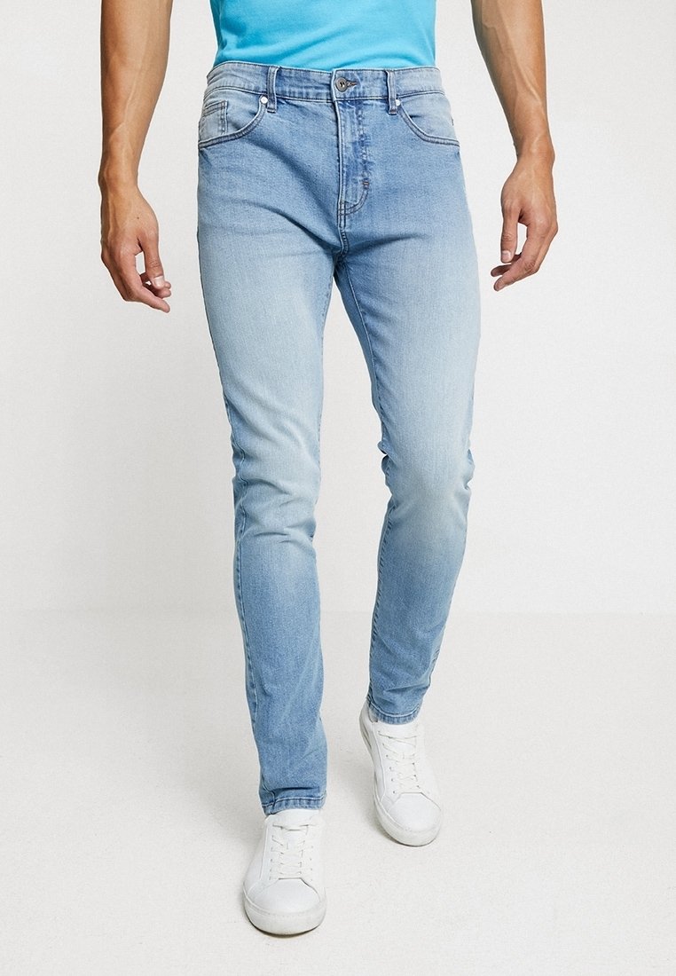 Ljusblå denimjeans med smal passform, som har framfickor, subtil blekning och knappgylf. Bärs med vita sneakers.