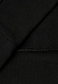 Černá pletená látka s jemnými a strukturovanými vzory. Měkký materiál s hladkým povrchem a kontrastním prošíváním podél okraje.