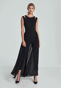Zwarte jurk met een nauwsluitend lijfje en een vloeiend doorschijnend rok, met een mouwloos ontwerp en uitsnijdingen op de schouders. Zachte textuur.