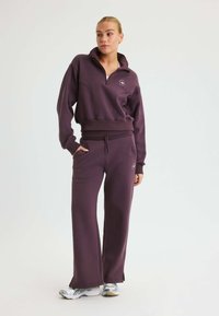 Lila sweatshirt med kvartdragkedja och sidofickor, ihop med matchande lila joggers med dragsko i midjan och utställd ham.