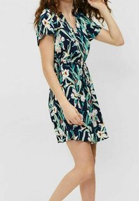 Blumenkleid aus navyblauem Stoff, mit V-Ausschnitt, kurzen Ärmeln und tailliertem Schnitt sowie einem weit ausgestellten Rock. Mit einem weißen und grünen Blumenmuster.