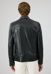 Zwarte leren jas met een getailleerd ontwerp, gladde textuur en ritsmanchetten. Geen opvallende hardware of patronen.