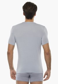 T-shirt grigio chiaro a maniche corte, texture liscia, scollo a giro, design aderente, indossato con pantaloni corti grigi coordinati, che mostrano uno stile minimalista.