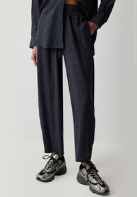 Dark plaid wide-leg pants with elastic waistband, paired with black and silver sneakers. Smooth fabric with a relaxed fit.