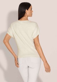 Lichtbeige korte mouwen trui met een ontspannen pasvorm, geribde halslijn en zoom, gecombineerd met lichtgrijze slim-fit broek. Gladde textuur.