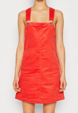 Rotes Corduroy-Trägerkleid mit verstellbaren Schulterträgern, Fronttaschen und einem ausgestellten Saum; strukturierte Oberfläche mit vertikalen Rillen.