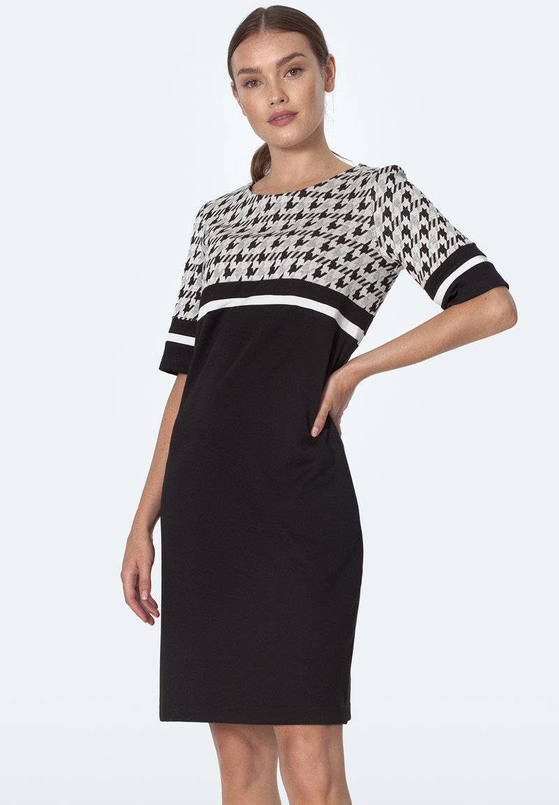 Czarna sukienka z górną częścią w wzór houndstooth, krótkimi rękawami i białym poziomym pasem. Gładki materiał, długość do kolan.