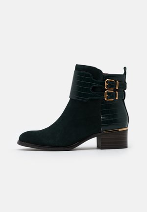 Groene suède enkellaars met krokodillenleeraccenten en twee gouden gespen. Heeft een gestapelde houten hak en een afgeronde neus.