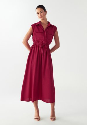 Burgundin värinen hihaton mekko, jossa on nappisuljenta edessä, kaksi rintataskua, vyötäröltä kireä malli ja virtaava puolipitkä hameosa. Silkkinen kangas.