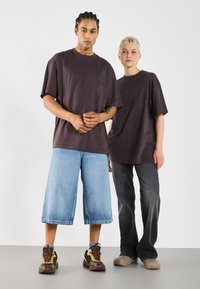 Mørkegrå oversized t-shirts med grafiske detaljer, blå vide jeans og forskelligt fodtøj; personer, der viser en afslappet streetwear stil.