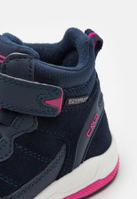 Navy vanntette sneakers med overdel i semsket skinn og tekstil, rosa aksenter, polstret krage, justerbar borrelåsrem, og gummisåle med rosa detaljer.