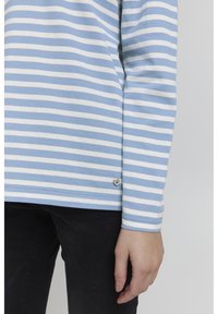 Kék és fehér csíkos, hosszú ujjú ing, puha tapintással, kis szív alakú kiegészítővel az alján, sötét nadrággal párosítva.