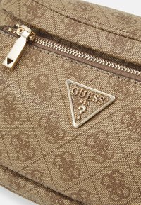 Pouch in tessuto marrone con motivo in rilievo, dotato di una cerniera dorata e logo triangolare Guess in oro. Texture liscia con una leggera lucentezza.