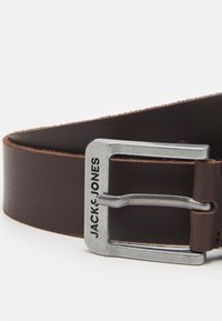 Cinturón de cuero marrón con una hebilla rectangular plateada, con el nombre de la marca "JACK & JONES" grabado en la hebilla. Textura suave.