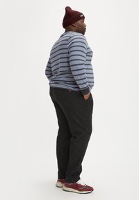 Gestreepte langemouwen shirt in navy en lichtblauw, donkere broek en bordeauxrode gebreide muts. Sneakers hebben een rood en grijs patroon.