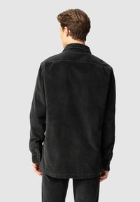 Camicia in corduroy nera con colletto, maniche lunghe e polsini con bottoni. Presenta una texture a coste e una vestibilità leggermente oversize.