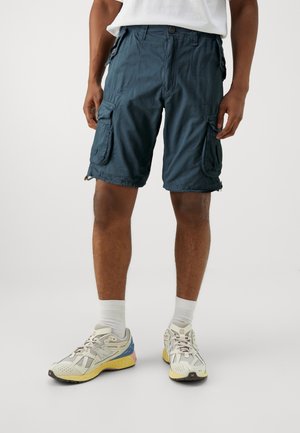 Shorts cargo bleu canard foncé avec plusieurs poches latérales, une fermeture à bouton et une coupe décontractée, fabriqués en tissu léger. Portés avec des baskets.