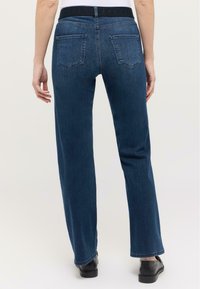 Blugi din denim albastru cu croi dreapt, având un tiv negru și două buzunare la spate. Materialul are o textură netedă, cu detalii minime.
