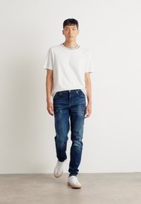 Tricou alb cu guler rotund și accente negre, asociat cu blugi bleumarin cu detalii decolorate. Modelul poartă adidași albi cu tălpi din cauciuc.
